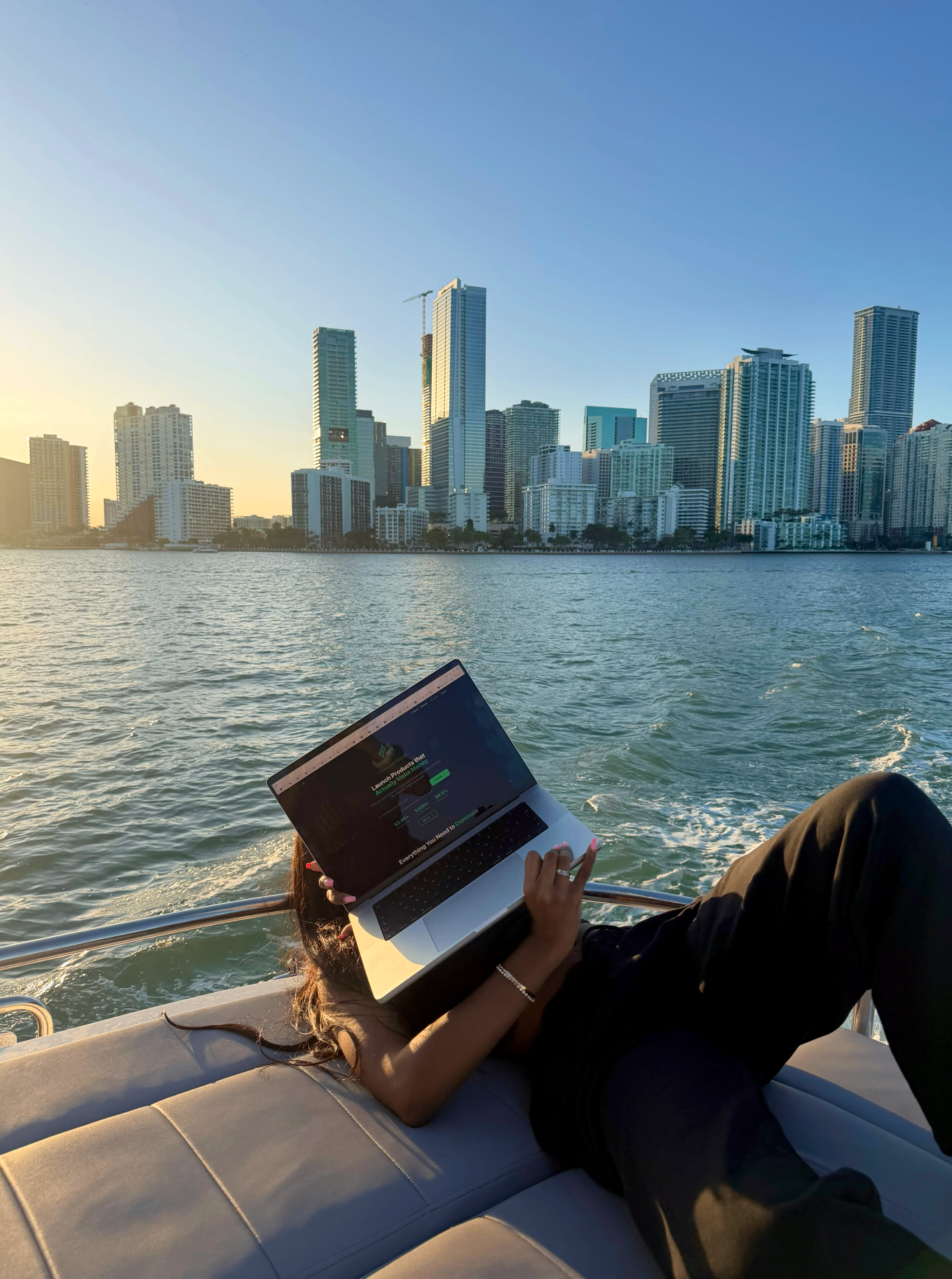 Monrae Hou working on a laptop on a boat with the Miami skyline at sunset